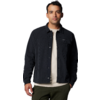 Staande man kijkt in de camera, draagt een zwarte overshirt over een wit T-shirt en een olijfgroene broek voor een witte achtergrond