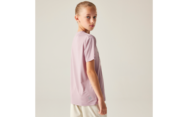 Person mit blondem Pferdeschwanz, trägt ein hellrosa kurzärmeliges Shirt und weiße Shorts, seitlich gedreht und schaut über die Schulter vor hellem einfarbigem Hintergrund