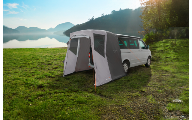 Graues Vorzelt an einem weißen Campingbus befestigt, mit geöffnetem Eingang und gespannten Abspannleinen