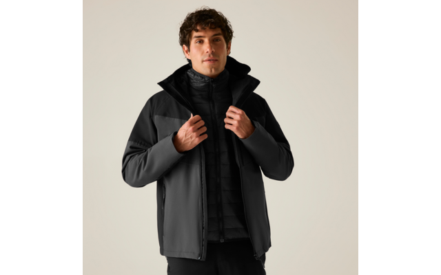 Person mit dunkler Softshelljacke und gesteppter Innenjacke, Hände am Reißverschluss, heller einfarbiger Hintergrund