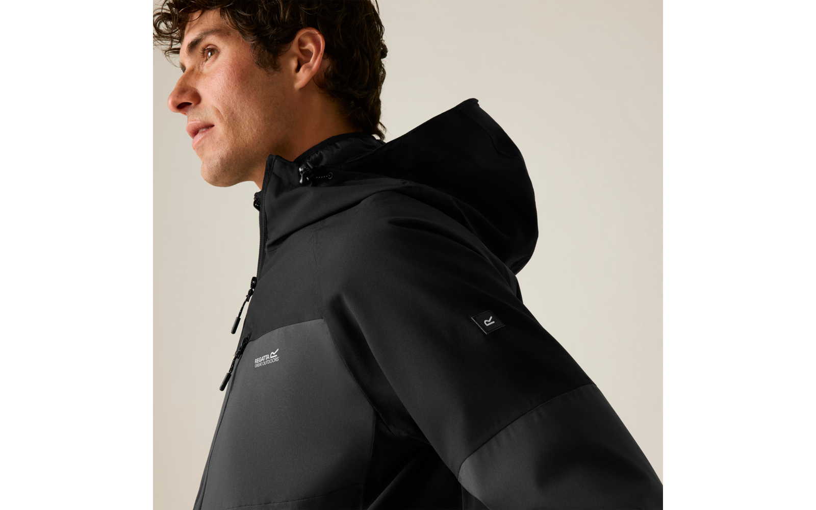 Seitenansicht eines Mannes in schwarzer Kapuzenjacke mit Reißverschluss und kleinem Logo auf dem Ärmel, er schaut nach links
