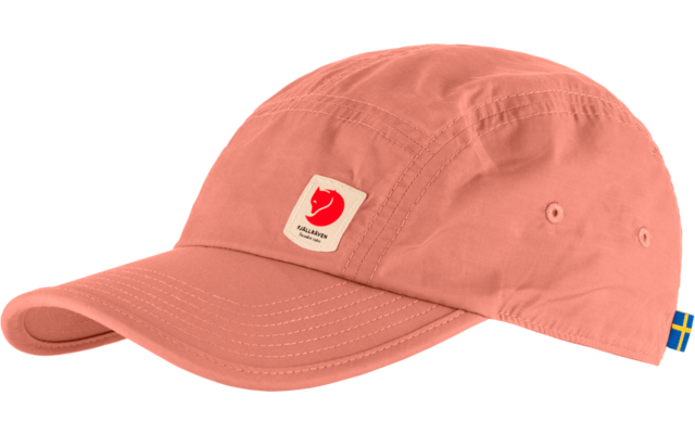 Korallenfarbene Kappe mit gebogenem Schirm, weißes quadratisches Etikett mit rotem Motiv und schwarzem Text vorne, kleines schwedisches Fähnchen an der Rückseite