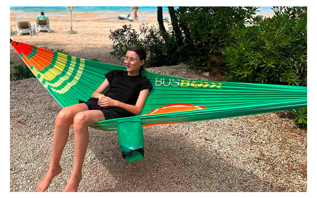 Frau sitzt auf einer grünen Hängematte am Strand mit Meer im Hintergrund