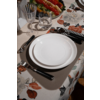 Table with white plate on beige placemat, cutlery with black handles, water glass and wine glass, floral tablecloth and serving dish with red and yellow bell peppers