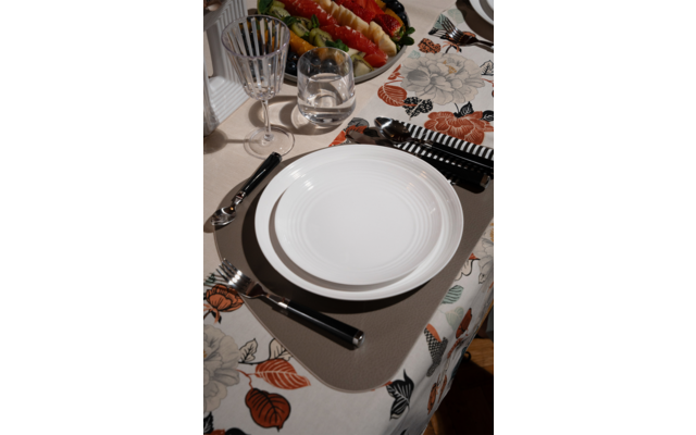 Table with white plate on beige placemat, cutlery with black handles, water glass and wine glass, floral tablecloth and serving dish with red and yellow bell peppers
