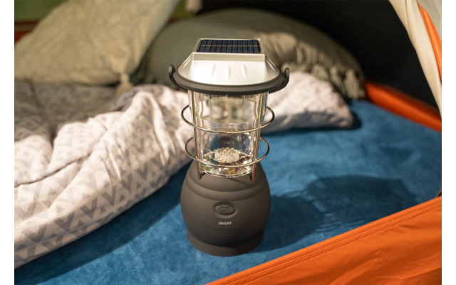 Schwarze Laterne mit Solarpanel und Glaskolben auf blauer Isomatte in einem orangefarbenen Zelt