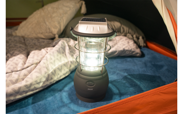 Helle Laterne auf blauer Schlafunterlage in einem orangefarbenen Zelt, daneben Kopfkissen und gemusterte Decke