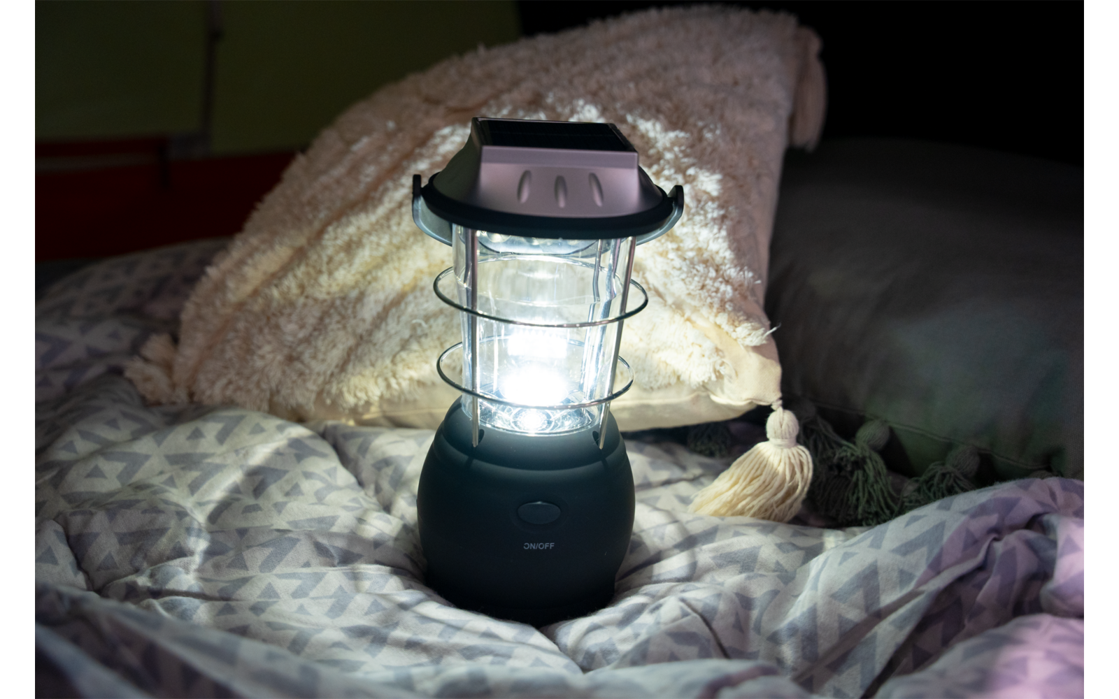 Eine leuchtende Laterne steht auf einem Bett mit gemustertem Bettbezug und einem Kissen mit Quaste