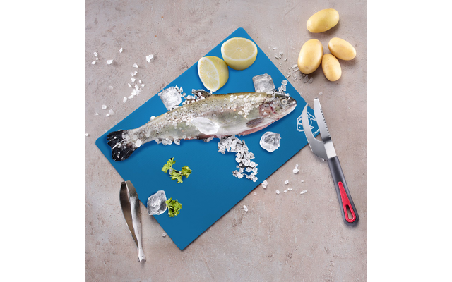Fish with coarse salt on a blue cutting board, lemon halves, ice cubes, parsley sprigs, three small potatoes, knife with black and red handle and tongs on a light surface