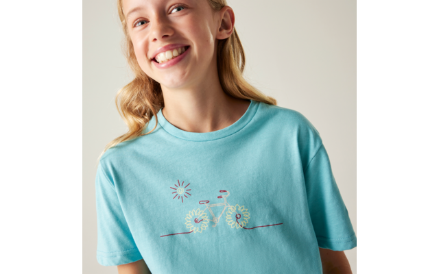 Oberkörper einer lächelnden Person in hellblauem T-Shirt mit aufgesticktem Fahrrad aus Blumen und kleinem Sonnenmotiv