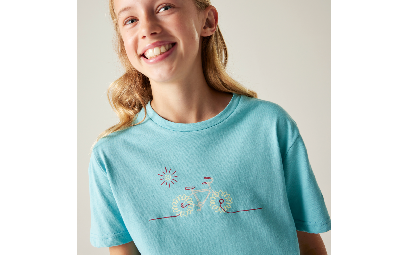 Oberkörper einer lächelnden Person in hellblauem T-Shirt mit aufgesticktem Fahrrad aus Blumen und kleinem Sonnenmotiv