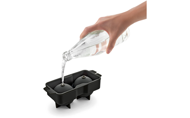 Hand gießt Wasser in eine schwarze Eiskastenform mit Eiswürfelfächern