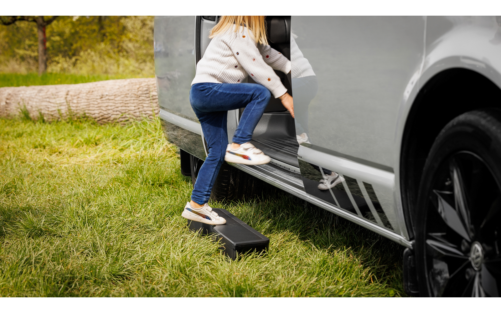 Kind steigt mit Hilfe eines kleinen Hockers in ein Fahrzeug ein