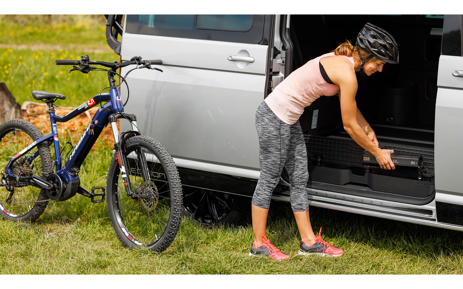 Frau in Sportkleidung neben Fahrrad vor geöffnetem Van