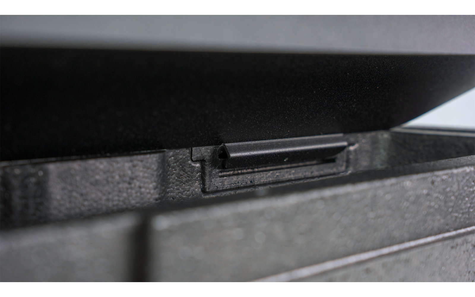 Nahaufnahme eines schwarzen Kunststoffteils mit rechteckigem Schlitz auf einer strukturierten Oberfläche