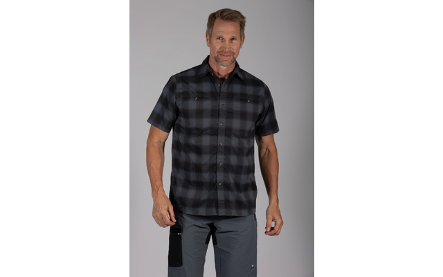 Man staand, gefotografeerd van voren, draagt een zwart-grijs geruit overhemd met korte mouwen en een grijze broek, neutrale lichtgrijze achtergrond