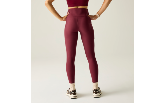 Vista trasera de una persona con mallas burdeos y top deportivo a juego, manos en las caderas, calcetines blancos y zapatillas deportivas negras, fondo claro