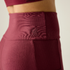 Primer plano lateral de la cintura de una persona con leggings burdeos acanalados de talle alto y un top deportivo a juego