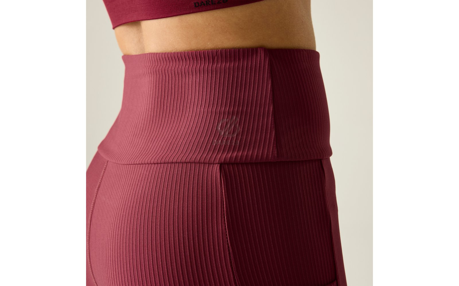 Primer plano lateral de la cintura de una persona con leggings burdeos acanalados de talle alto y un top deportivo a juego