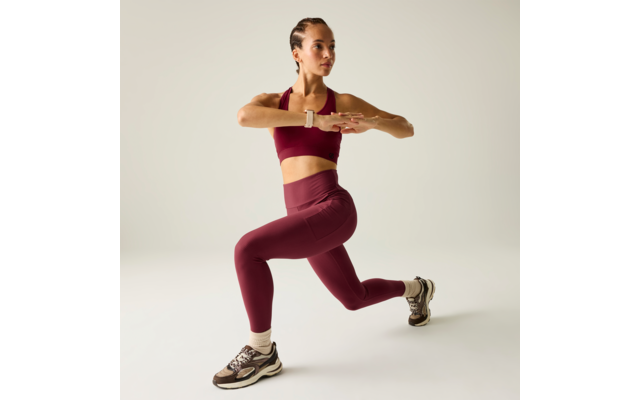Persona con ropa deportiva burdeos, pierna delantera doblada, pierna trasera estirada, brazos sobre el pecho, zapatillas claras, fondo claro