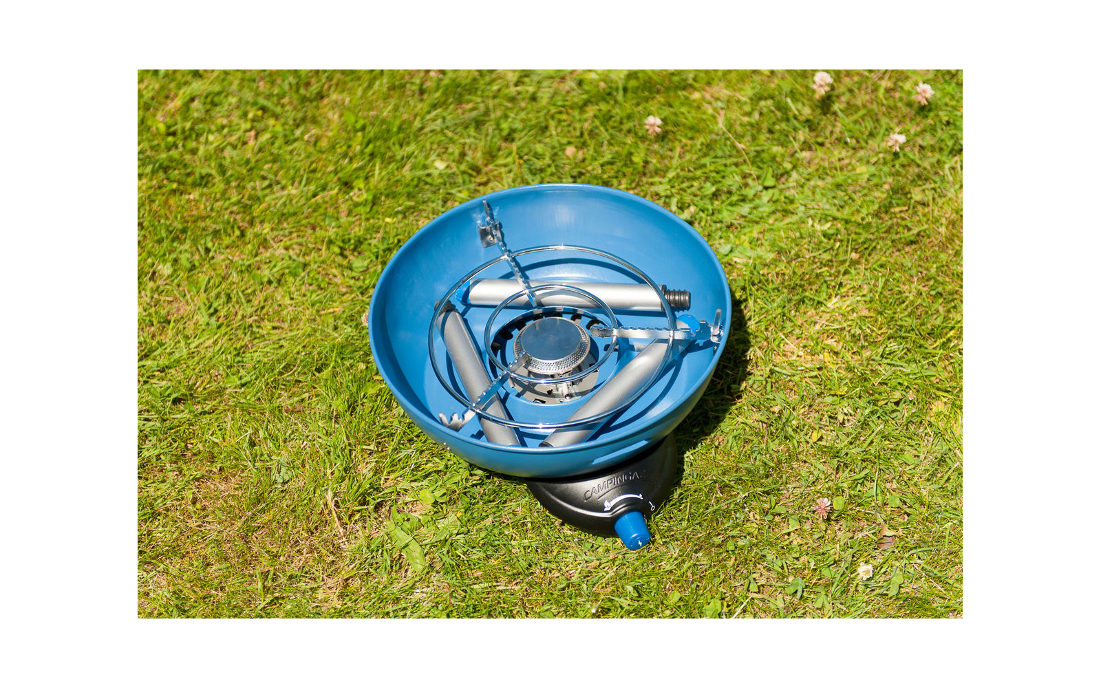 Blauwe eenpit gasbrander met ronde pannendrager en blauwe aansluiting op gras