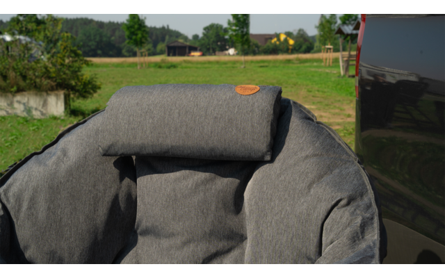 Grauer gepolsterter Sitz mit Kopfstütze im Freien vor einer grünen Wiese und Bäumen