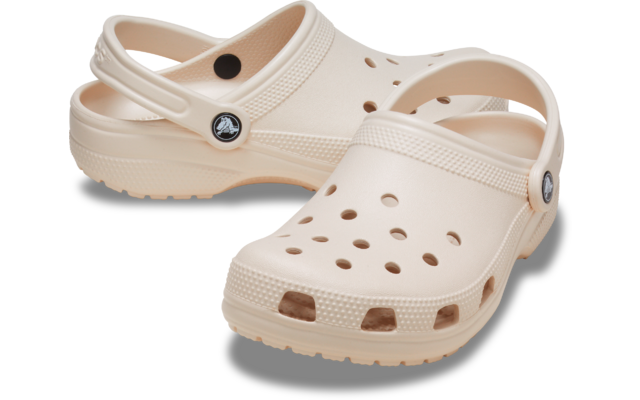 Ein Paar hellbeige Kunststoff‑Clogs mit Lüftungsöffnungen, Fersenriemen, genoppter Sohle und rundem Zierknopf an der Seite