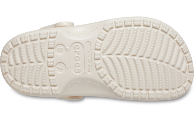 Unterseite einer cremefarbenen Crocs-Schuhsohle mit Profilrillen und geprägtem Markenlogo