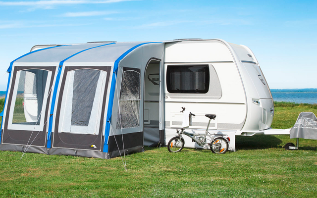Caravane blanche avec auvent attaché et vélo d'enfant sur l'herbe verte sous un ciel clair