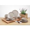 Verschiedene Teller und Schalen aus Keramik auf einem Holztisch, daneben ein Besteckset und ein Holzkasten mit Pflanzen