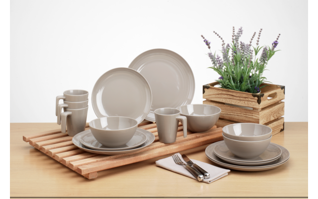 Verschiedene Teller und Schalen aus Keramik auf einem Holztisch, daneben ein Besteckset und ein Holzkasten mit Pflanzen