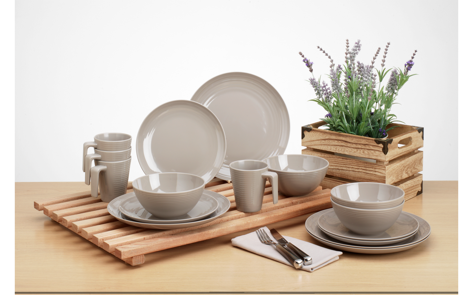 Verschiedene Teller und Schalen aus Keramik auf einem Holztisch, daneben ein Besteckset und ein Holzkasten mit Pflanzen