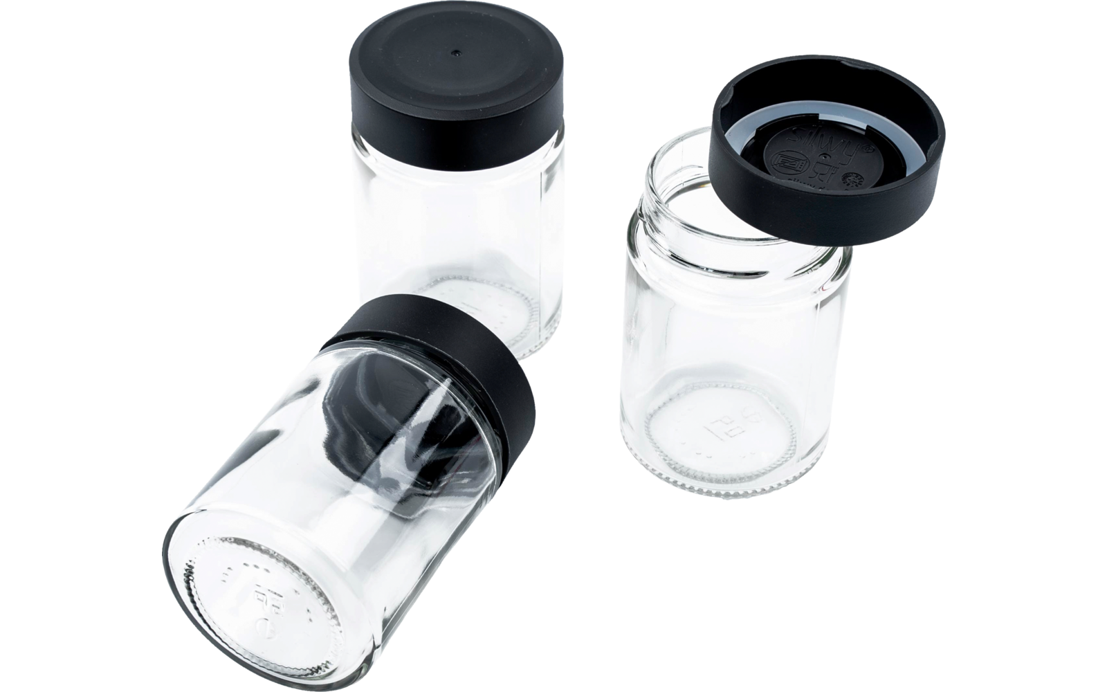 Drei transparente Glasbehälter mit schwarzen Deckeln; eines liegt auf der Seite, eines steht mit Deckel, eines steht offen mit Deckel daneben