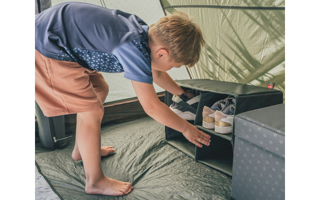 Un bambino a piedi nudi dentro una tenda si china per mettere scarpe in un organizer per scarpe nero