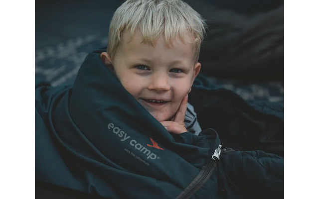 Junge mit blondem Haar, der in einem Schlafsack liegt und in die Kamera lächelt
