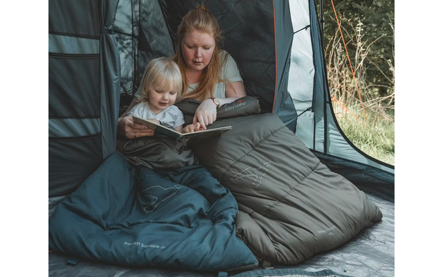 Frau liest zwei kleinen Kindern aus einem Buch vor, alle sitzen in einem Schlafsack in einem Zelt