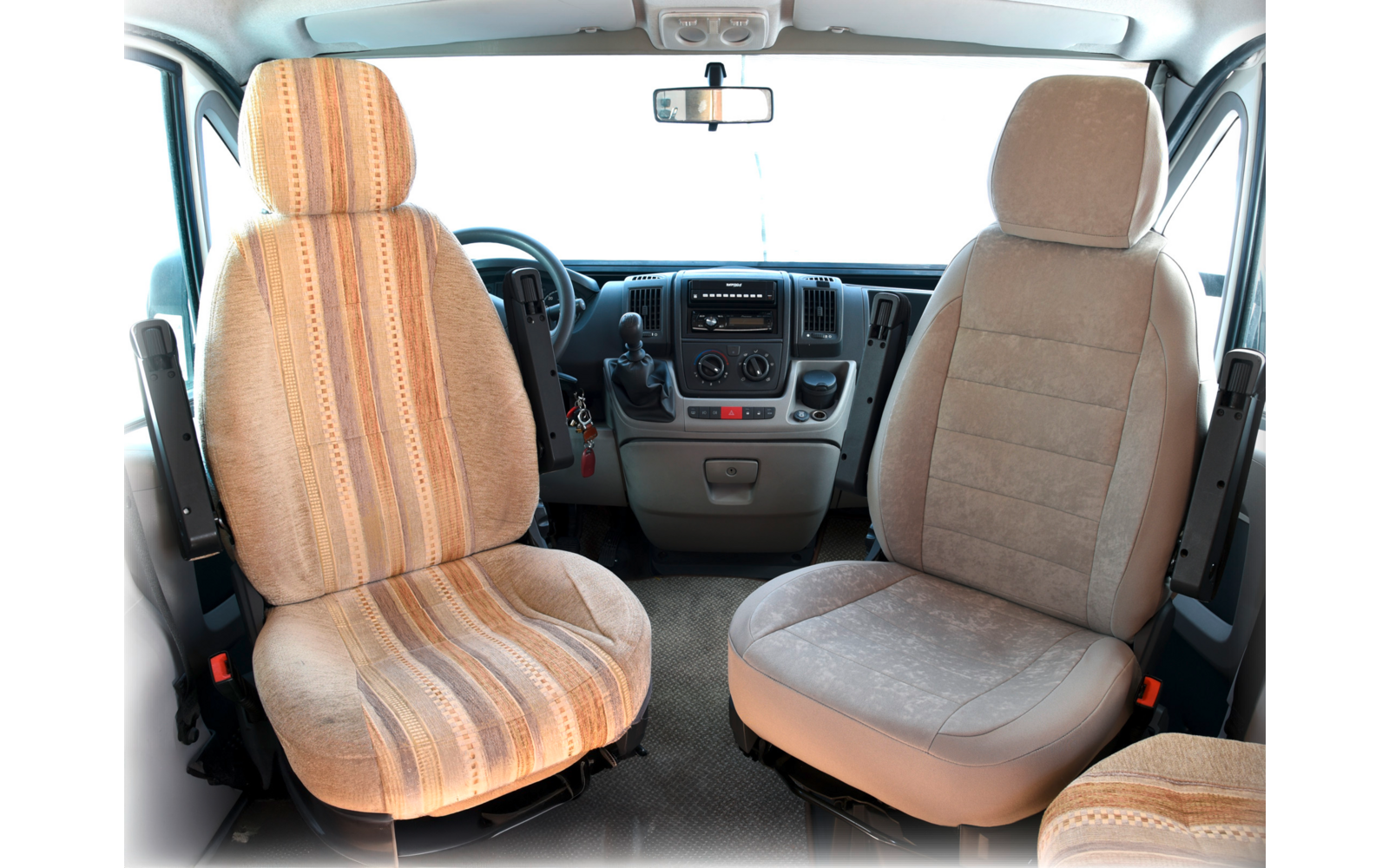 Two front seats in a vehicle, left with striped fabric cover, right with solid fabric cover, steering wheel and dashboard in the background