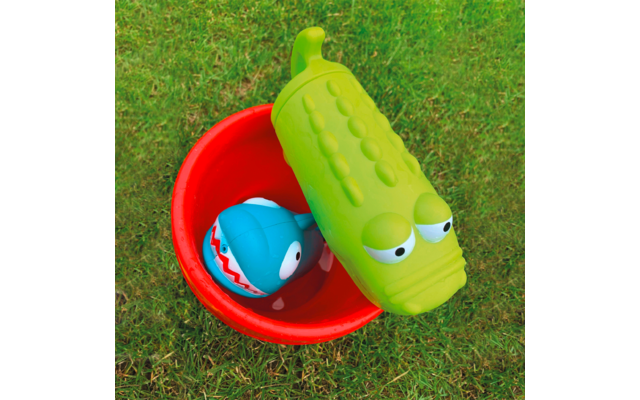 Grüne Spielzeug-Krokodildecke über rotem Eimer mit blauem Spielzeugfisch auf grünem Gras