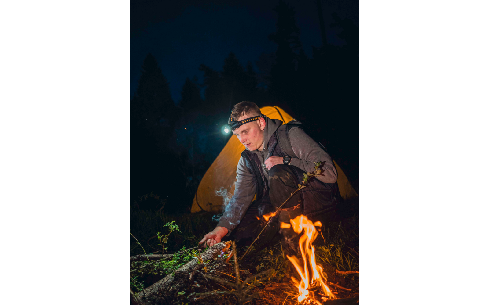 Mann zündet am Lagerfeuer eine Fackel an, Nacht im Wald