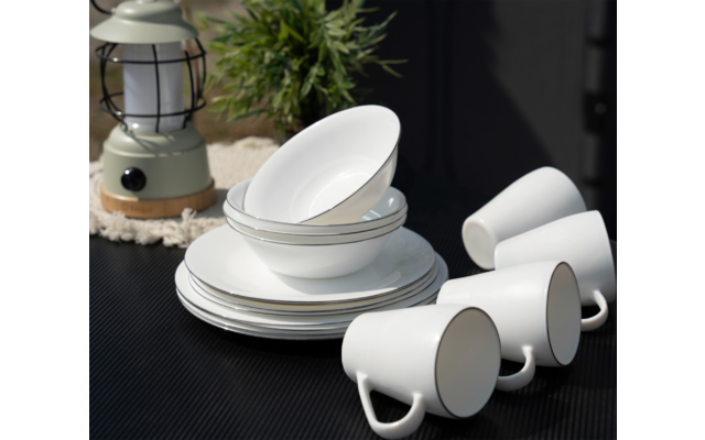 Gestapelte weiße Teller und Schalen neben drei weißen Tassen auf dunklem Untergrund, im Hintergrund eine Laterne und eine Pflanze