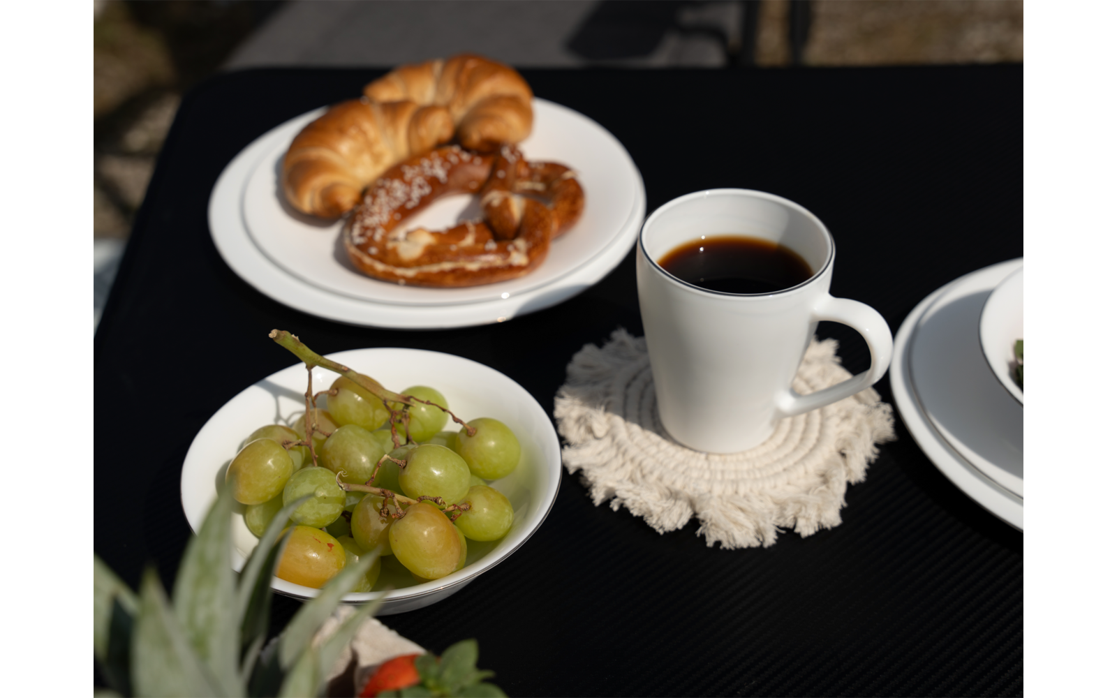 Ein Tisch mit einer Tasse Kaffee, einem Teller mit Croissants und einem Teller mit Trauben