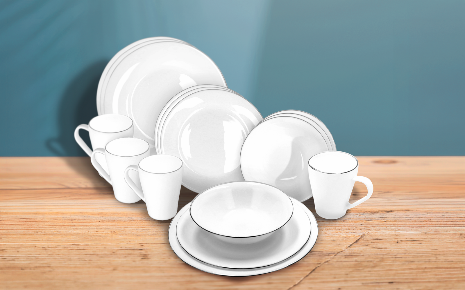 White dishes (plates, bowls, mugs) with a thin silver rim on a wooden table against a blue background