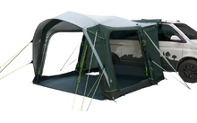 Tenda verde-grigio con ingresso aperto e pannelli laterali in rete, fissata a un furgone bianco, sfondo bianco
