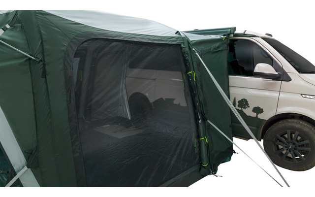 Grünes Vorzelt mit Moskitonetz und Reißverschluss, an der Seite eines weißen Campingbusses befestigt; vorderes Rad und Baumaufkleber sichtbar