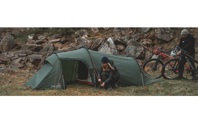 Zwei Personen sitzen vor einem grünen Zelt mit Fahrrädern im Hintergrund