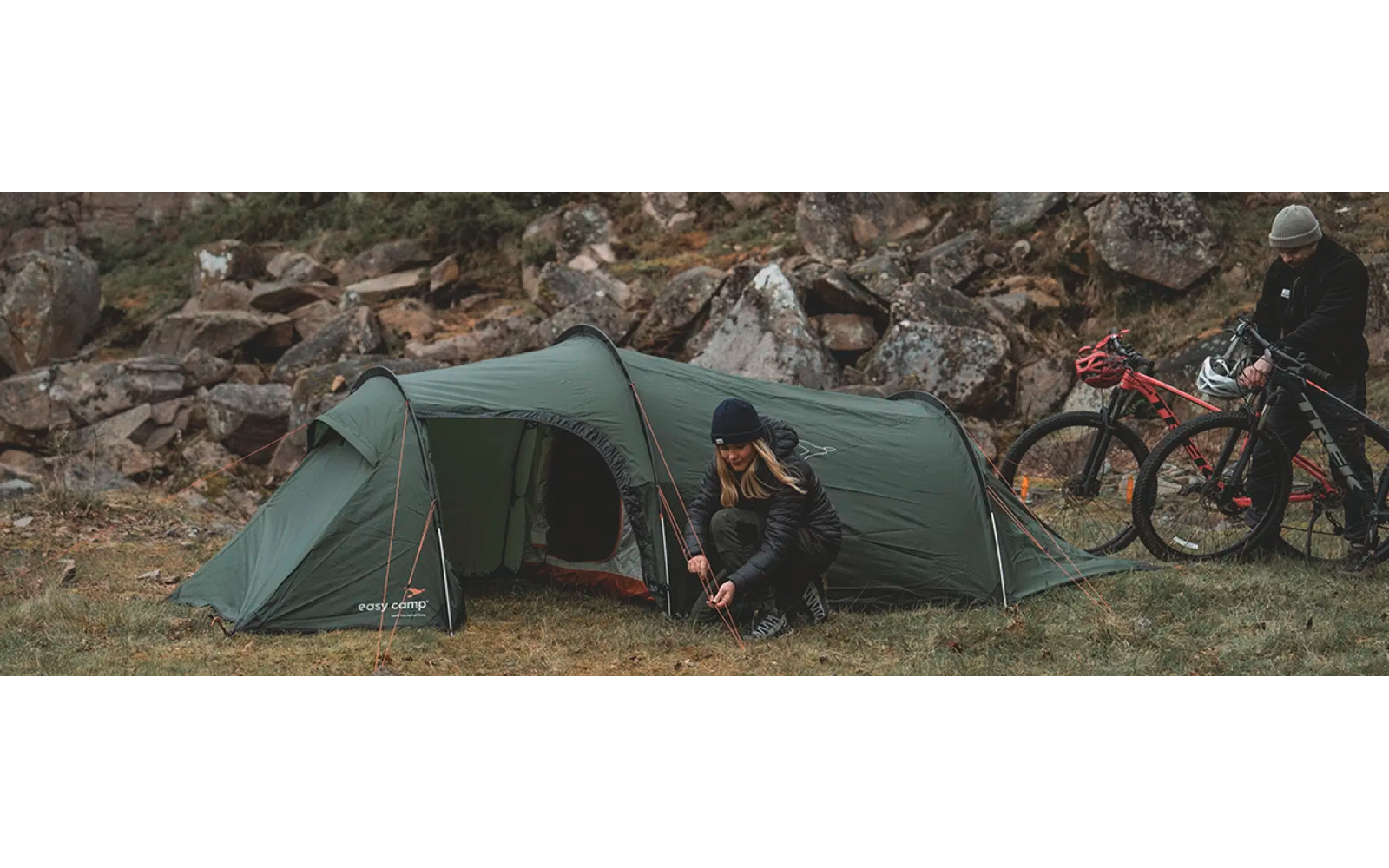 Zwei Personen sitzen vor einem grünen Zelt mit Fahrrädern im Hintergrund