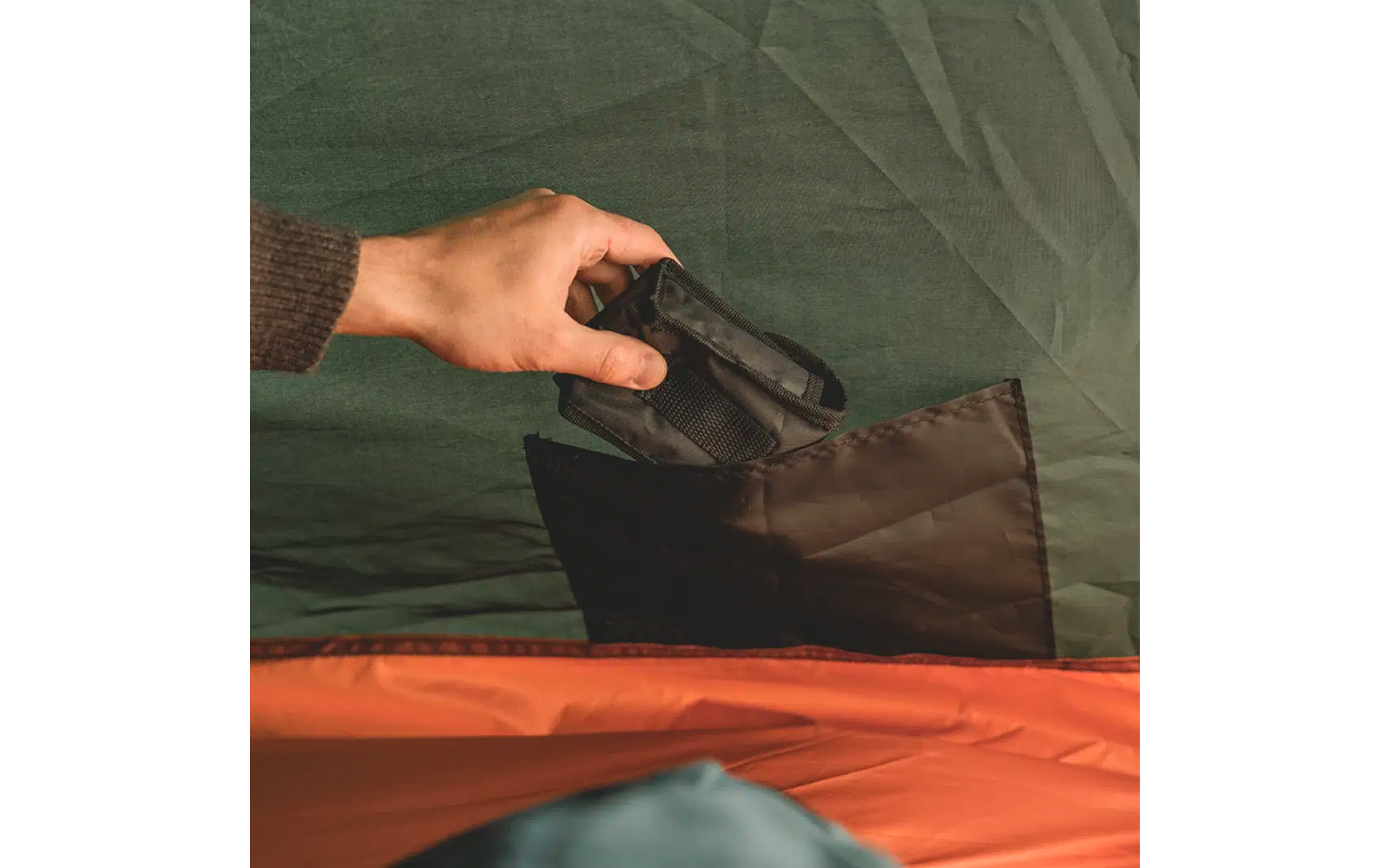 Hand legt Kamera in eine offene Tasche vor grünem Hintergrund