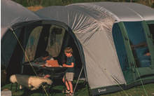 Zwei Kinder sitzen und spielen vor einem großen Zelt, ein Schwein steht in der Nähe