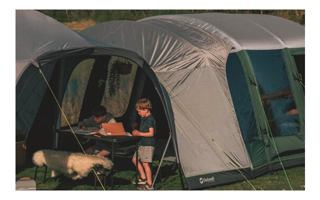 Zwei Kinder sitzen und spielen vor einem großen Zelt, ein Schwein steht in der Nähe