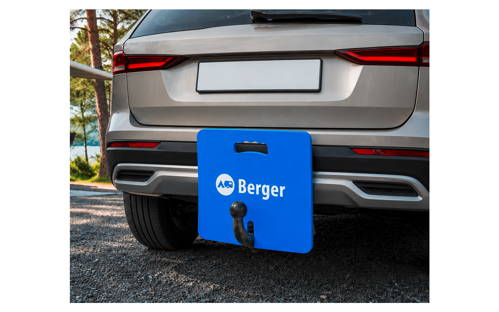 Achterkant van een zilverkleurige SUV met een witte kentekenplaat, een blauw bord met 'Berger' voor de trekhaak, zichtbare trekhaakkogel, asfalt en bomen op de achtergrond